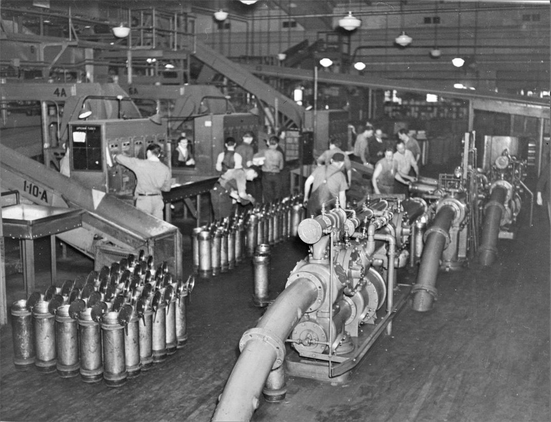A photograph of one of New York City’s post offices with pneumatic tubes. There are dozens of canisters lined up next to loading dozens, and a handful of workers ready to send them off.
